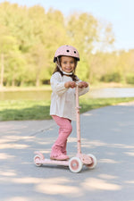 Child riding a pink scooter outdoors on a sunny day