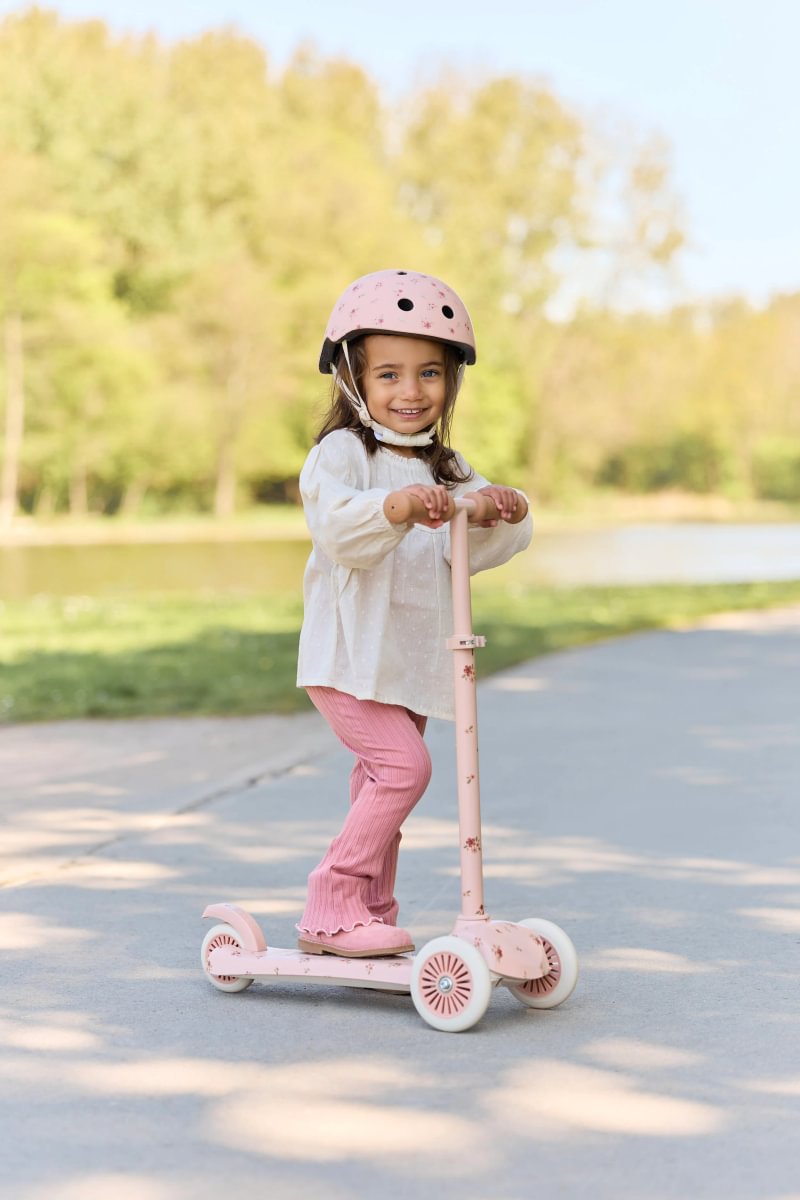 Child riding a pink scooter outdoors on a sunny day