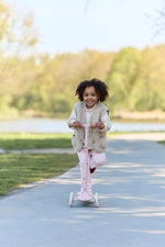 Child riding a scooter on a path with trees in the background